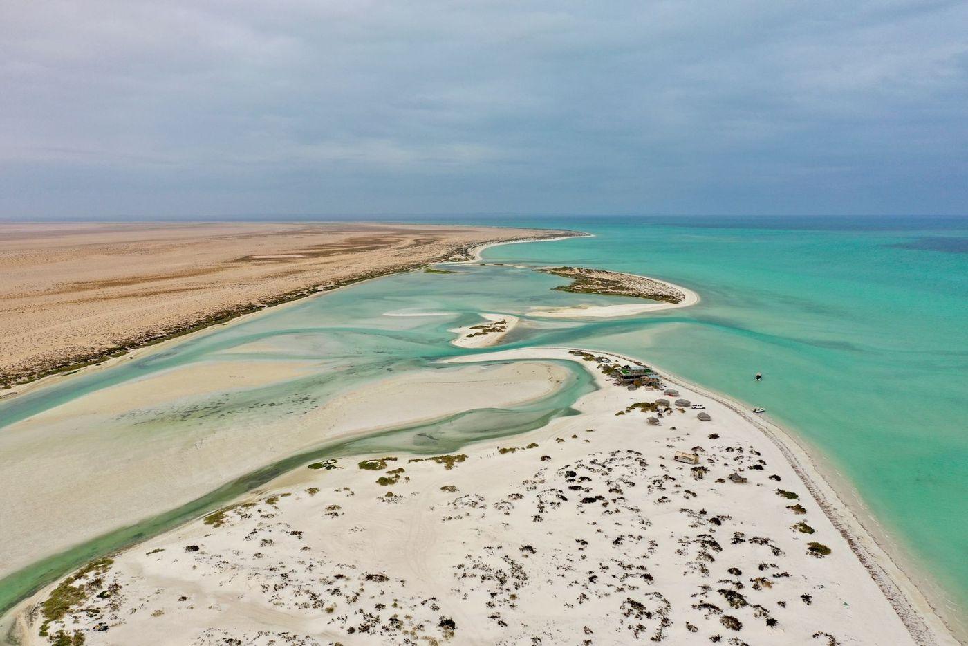 Aerial view of a remote arid coastline where pale sand meets turquoise water