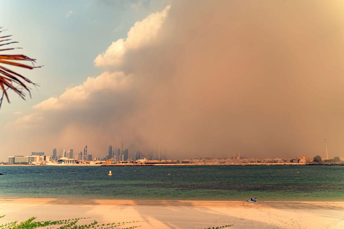 A wall of dust approaching a coastal skyline while the sea in front stays calm