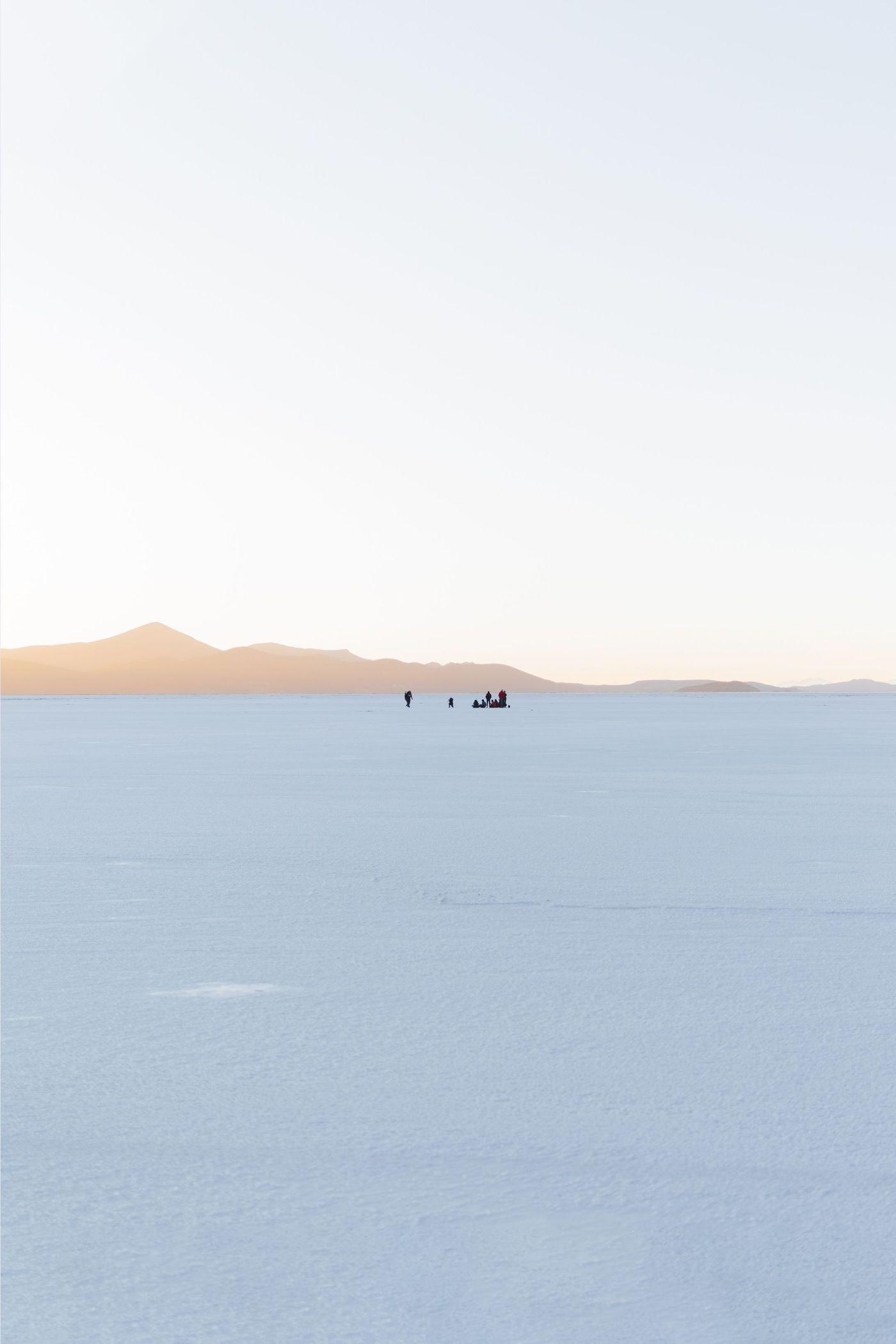 Sunrise over a salt flat with figures silhouetted in the distance